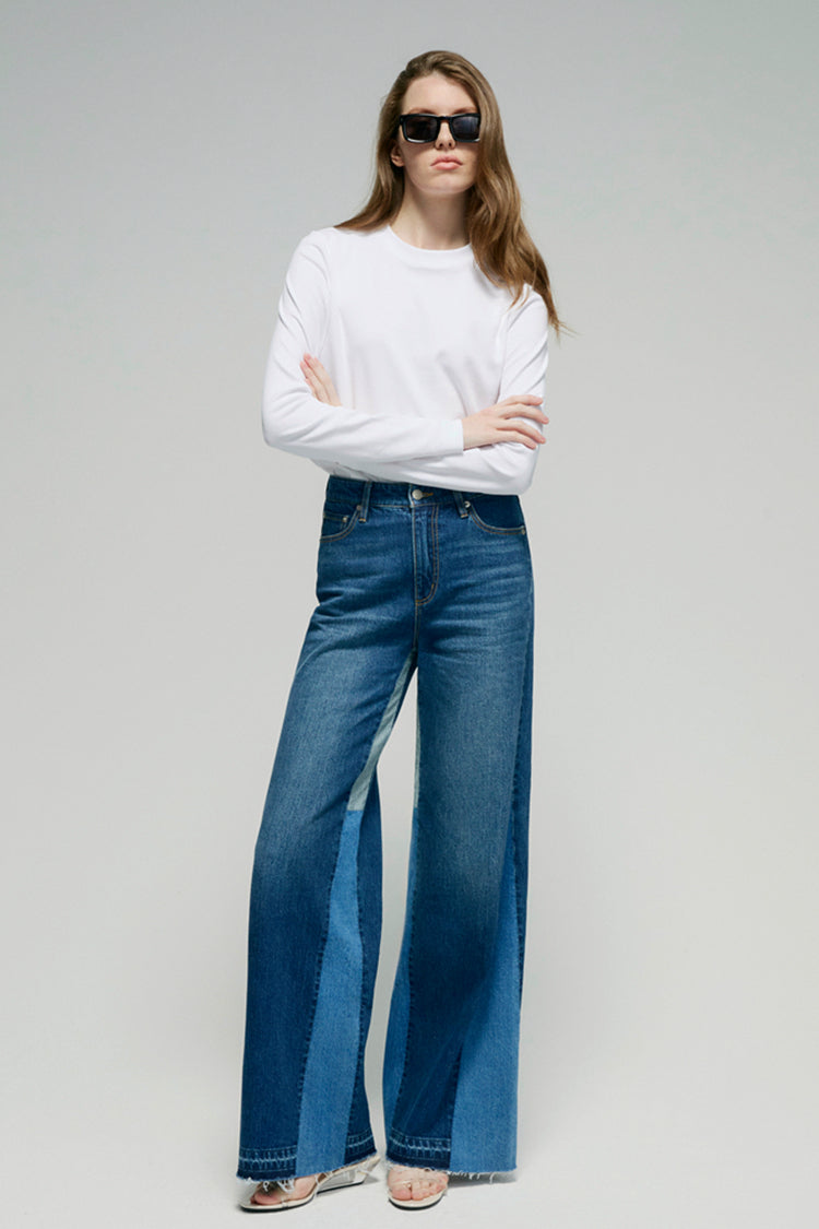 Woman wearing blue jeans and a white top on a plain background