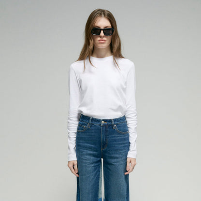 Person wearing a white long-sleeve shirt and blue jeans on a plain background