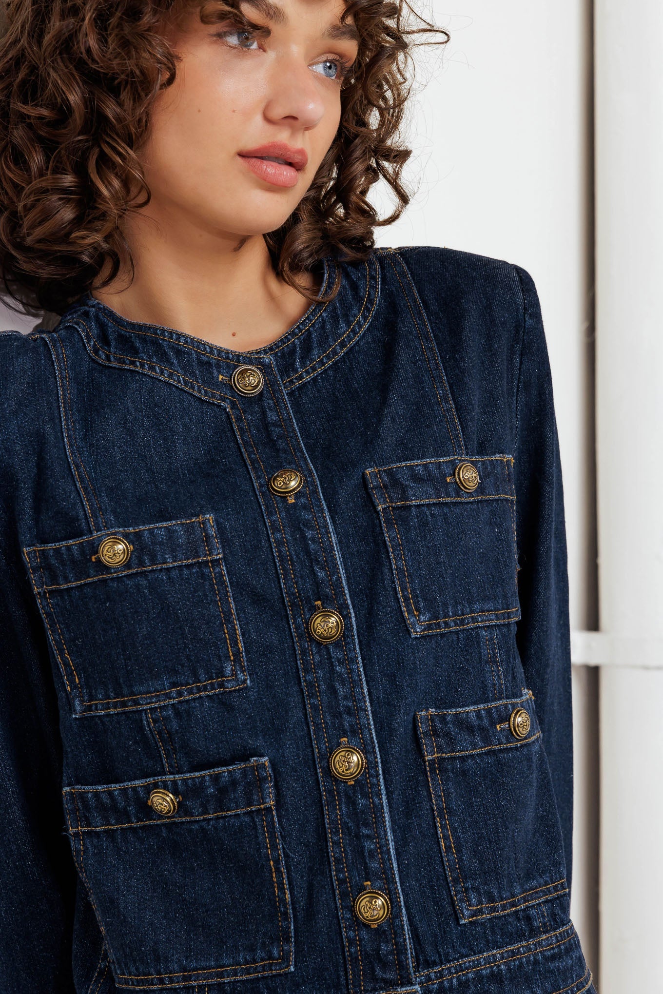 Person wearing a blue denim jacket with gold buttons against a white background