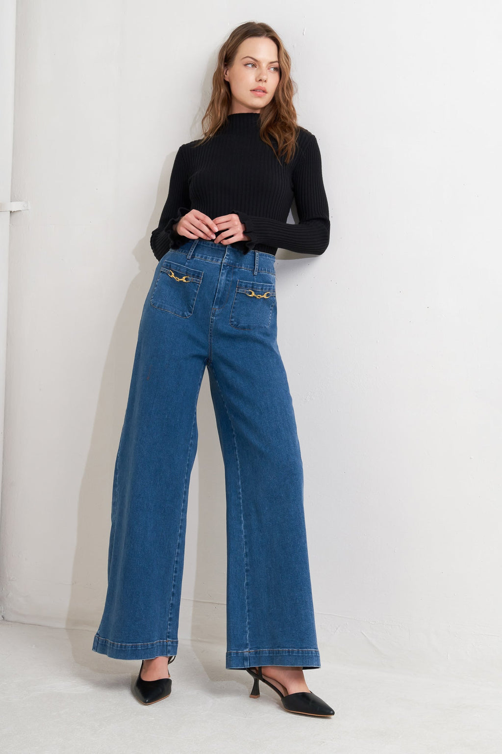 Woman wearing blue jeans and a black top against a white background
