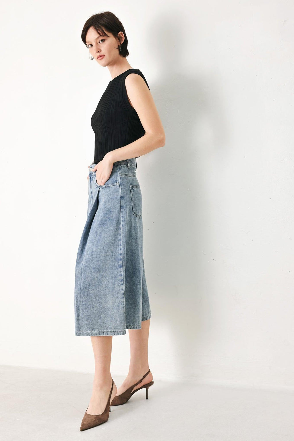 Woman wearing a black sleeveless top and denim skirt on a white background