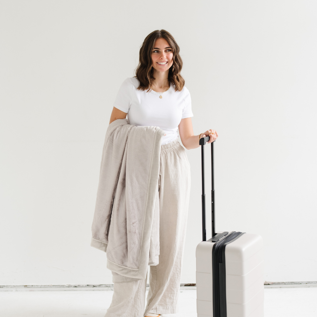 Woman holding a folded blanket and a suitcase in a minimalistic setting