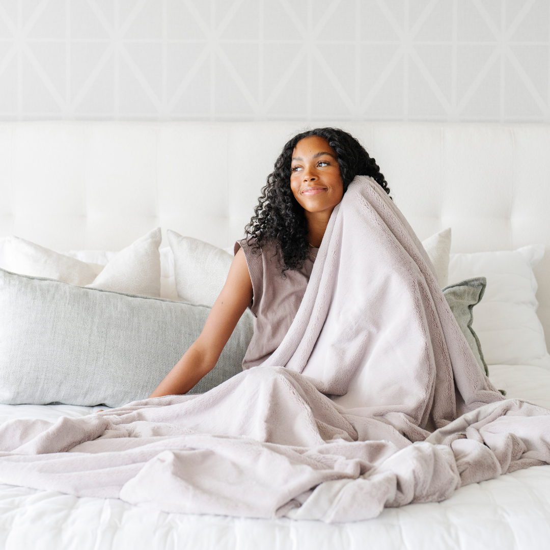 Woman wrapped in a blanket sitting on a bed in a cozy room.