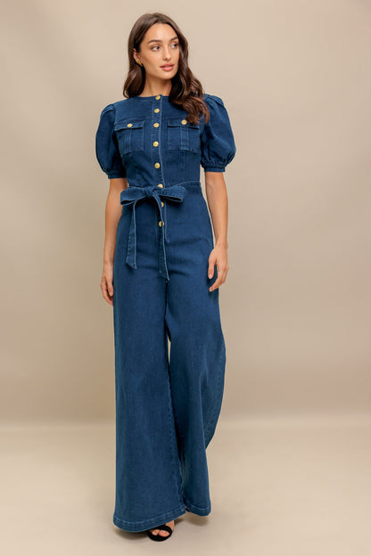 Woman wearing a blue denim jumpsuit against a beige background