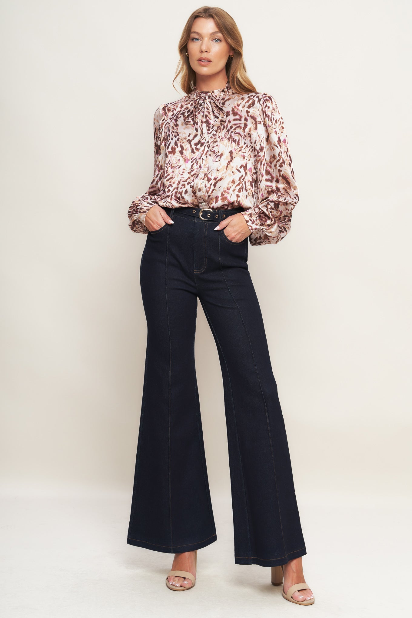 Woman wearing a patterned blouse and black flared pants on a white background