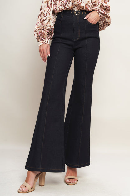 Person wearing black flared jeans and a patterned blouse on a plain background