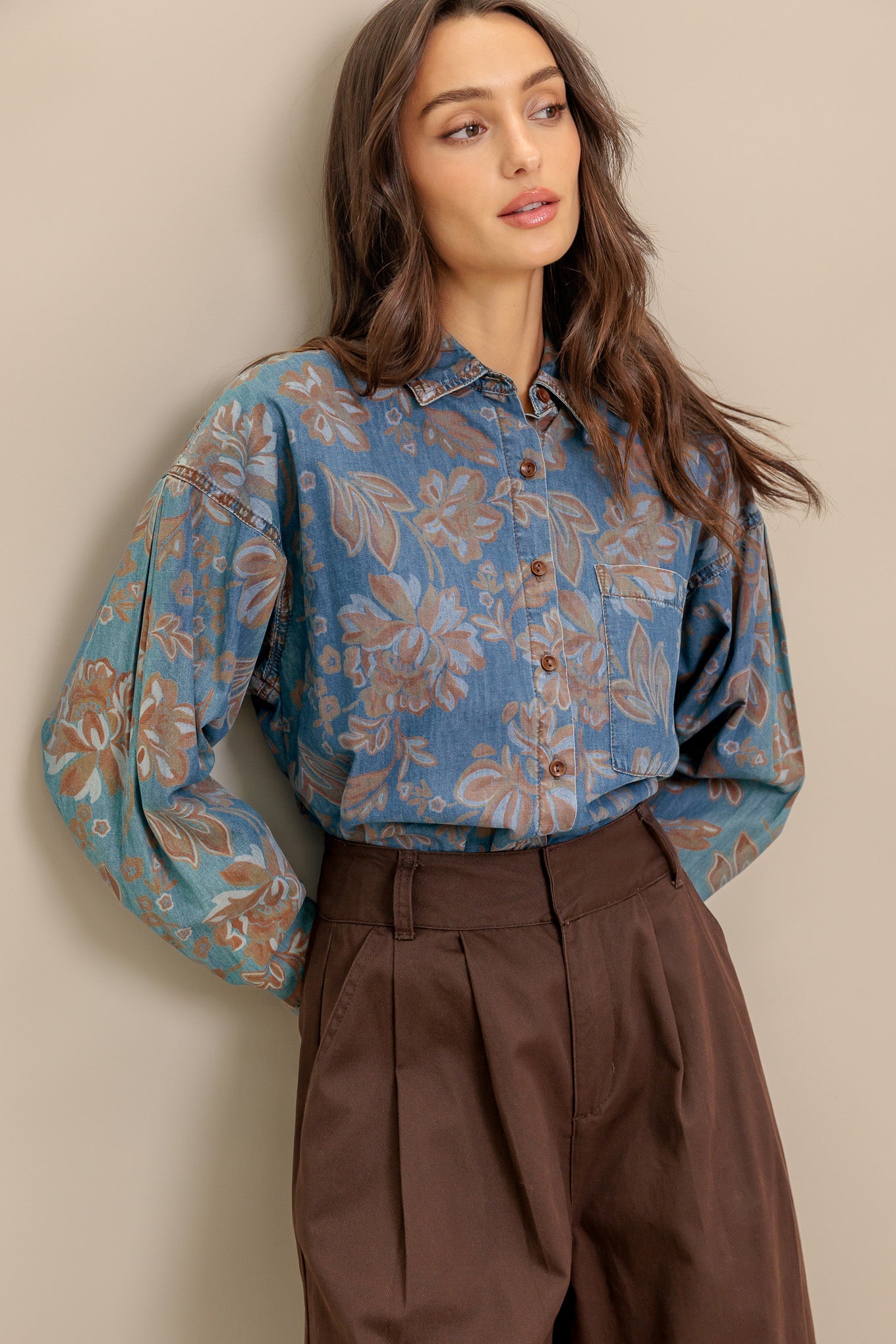 Woman wearing a blue floral blouse and brown pants against a beige wall