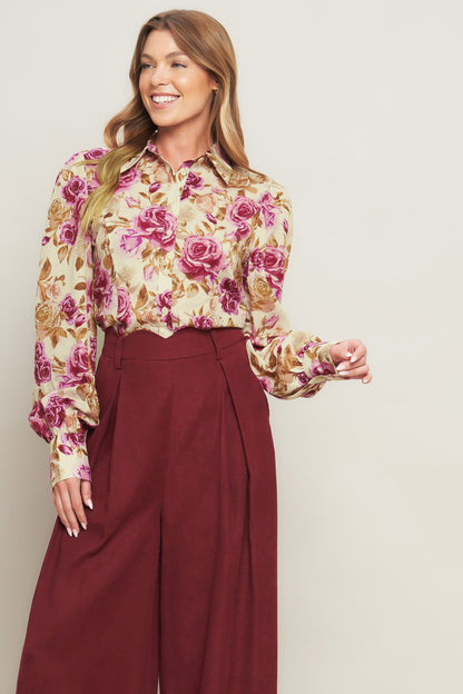Woman wearing a floral blouse and burgundy pants against a plain background