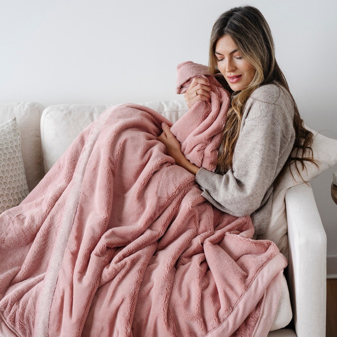 Woman wrapped in a pink blanket on a couch in a cozy living room.