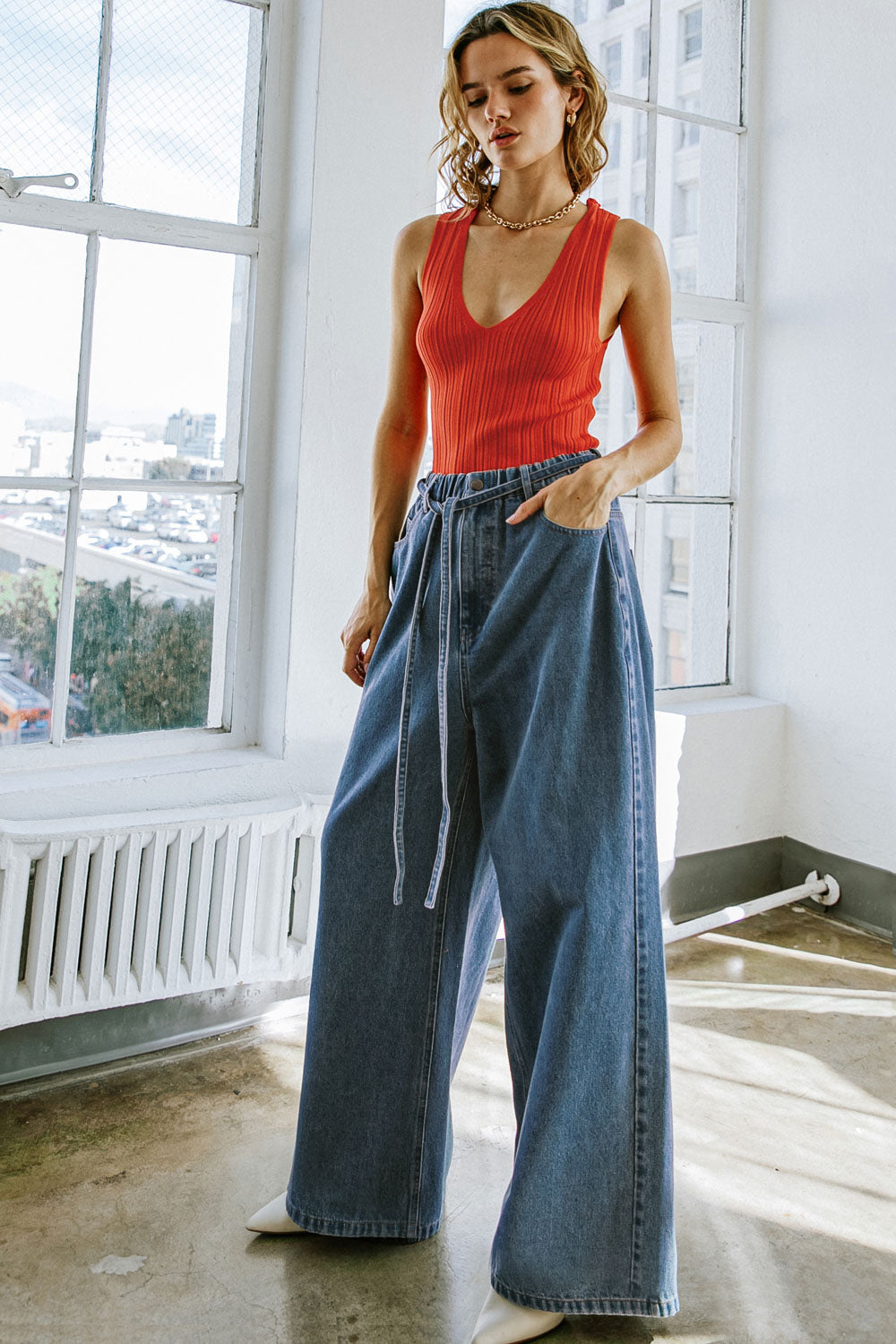 Woman wearing a red top and blue jeans in a bright room with large windows.
